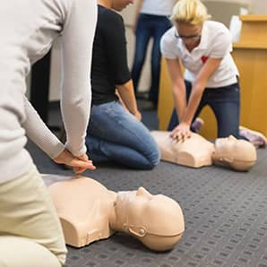 First aid CPR seminar. A group of adult education students practitcing CPR chest compressioon on a dummy.